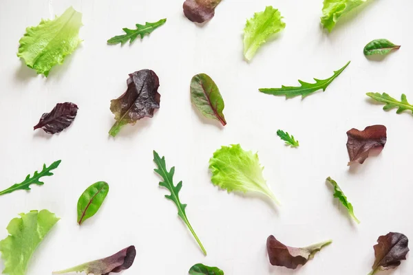 Green salad leaves on a white background. Pattern with lettuce leaves. Background design with leaves for salad. Pattern with lettuce leaves. Slimming, vegetarianism, organic food. Flat lay, top view.