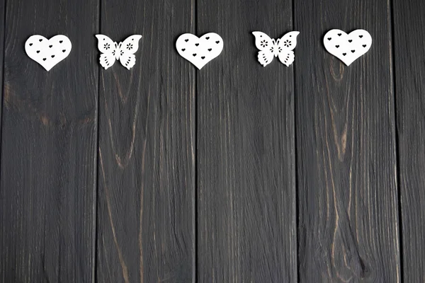 Weiße Holzherzen und Schmetterlinge auf grauem hölzernem Hintergrund. Blick von oben. Rahmen für Banner. Hintergrund für Grußkarte. — Stockfoto