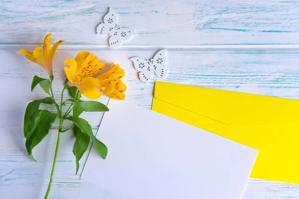 Kigúnyolják üres papírt és borítékot a fehér fa háttér természetes virágok sárga színű. Üres, szövegkeret. Üdvözlőlap virággal. Aalstroemeria. Lapos feküdt, felülnézet. — Stock Fotó