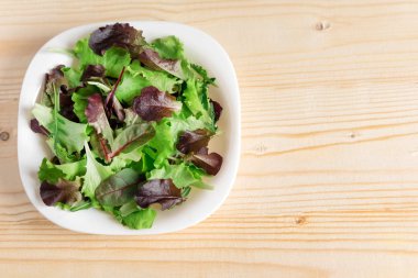 Ahşap bir arka plan üzerinde yeşil salata bir tabak ile bir afiş için Şablon. Sağlıklı yemekler, vejetaryenler, diyet. Yeşil salata bir tabak ile bir afiş için temel. Yukarıdan görüntüle