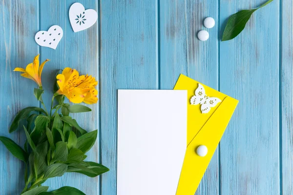 Kigúnyolják üres papír, e-mail borítékot a kék fa háttér természetes virágai sárga színű és pillangók. Üres, szövegkeret. Aalstroemeria fa háttérrel. Megtekintés felülről — Stock Fotó