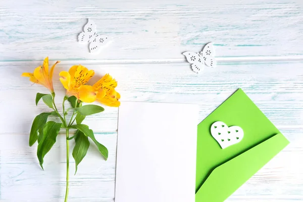 白い木製の背景に白い紙と封筒をモックアップし、黄色の自然な花を咲かせます。空白、テキストの枠。花とグリーティングカードのデザイン。フラットレイ、トップビュー. — ストック写真