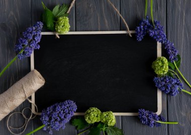 Gri ahşap arka plan üzerinde yazmak için bir tahta ile güzel mor ve yeşil çiçekler. Tebrik afişi, tebrik kartı için çerçeve. Düz döşeme, üst görünüm.