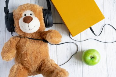 Kitabın fotoğrafları ve ona bağlı kulaklıklar. Sesli kitap. Uzaktan eğitim konusunda kavramsal fotoğraf. Öğrenmek için kitap dinleme.