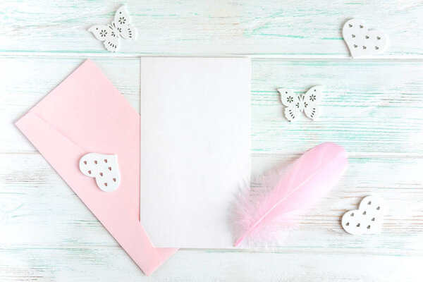 Mock up letter for greeting inscription. A letter on a light wooden background with a pink envelope, feather and spring flowers of the cherry tree.