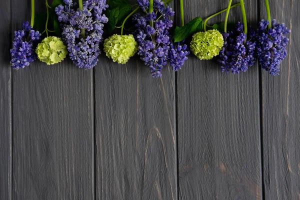 Schöne lila und grüne Blumen auf grauem Holzgrund mit Platz für die Grußbeschriftung. Rahmen für Grußbanner, Grußkarte. flache Lage, Draufsicht. — Stockfoto
