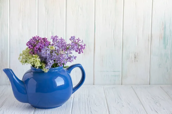 Flieder in einer blauen Teekanne mit einem Platz für eine Inschrift auf einem hölzernen Hintergrund. Fliederblüten — Stockfoto