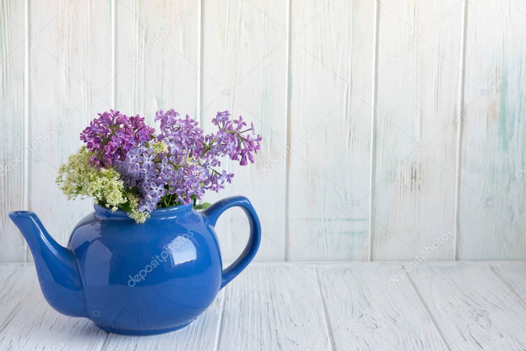 Lilac in a teapot of blue color with a place for an inscription on a wooden background. Lilac flowers