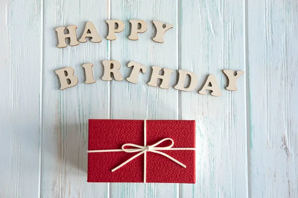 Happy Birthday. Greeting inscription from wooden letters on a light wooden background with a gift. Greeting card with a gift and the inscription. View from above
