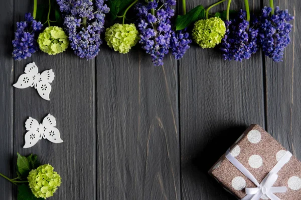 Όμορφα μωβ και πράσινα λουλούδια σε ένα γκρίζο ξύλινο φόντο με χώρο για ευχετήρια επιγραφή. Πλαίσιο για πανό χαιρετισμού, ευχετήρια κάρτα. Επίπεδη όψη, κορυφή θέα. — Φωτογραφία Αρχείου