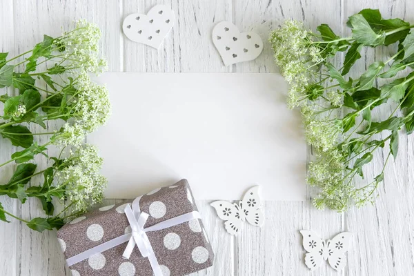 Hochzeitsgrußkarte-Attrappe mit grünen Blumen und Geschenk auf weißem Holzhintergrund. Rahmen für Grußkarte mit Blumen und Geschenk. Blumenbanner — Stockfoto