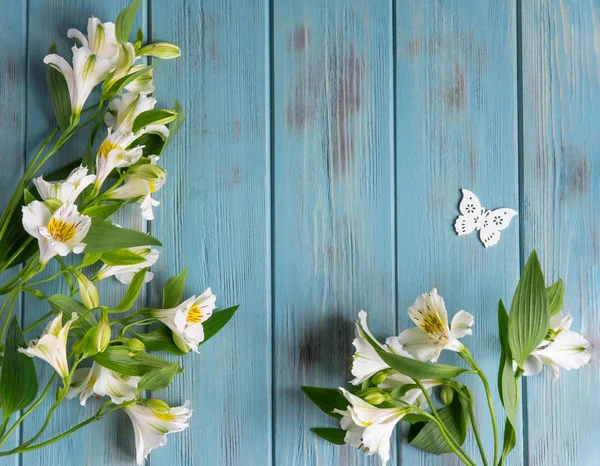 Background for text banner on a blue wooden background with white flowers and butterflies. Blank, frame for text. Greeting card design with flowers. Alstroemeria on wooden background. View from above