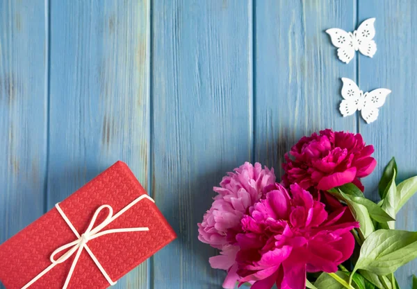 Marco para una tarjeta de felicitación con un ramo de peonías y un regalo sobre un fondo de madera azul. Peonías y un regalo con espacio para copyice. Vista de fondo floral desde la parte superior — Foto de Stock