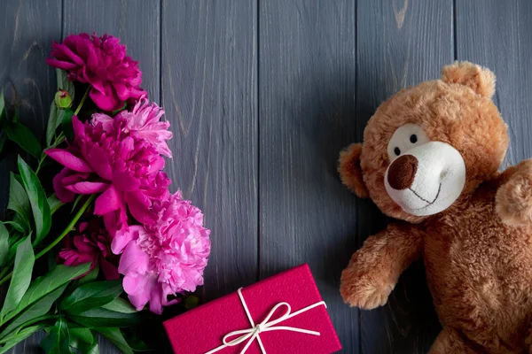 Un ramo de peonías sobre un fondo de madera con un regalo, un oso de juguete. Peonías rosadas y granate sobre un fondo oscuro. San Valentín y declaración de amor — Foto de Stock