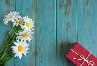 Ahşap bir arka plan ve bir hediye üzerinde papatyalar ile tebrik kartı için arka plan. Ahşap bir arka plan üzerinde papatyalar ile metin için çerçeve. Çiçek arka plan afişi. Düz döşeme, üst görünüm.