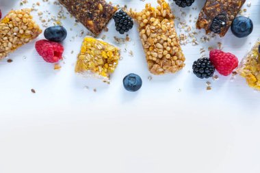 Beyaz ahşap arka plan üzerinde granola ve ahududu, böğürtlen, yaban mersini ve yulaf ezmesi doğal meyveleri ile metin için Çerçeve. Atıştırma ve kahvaltı için kullanışlı tahıl barları
