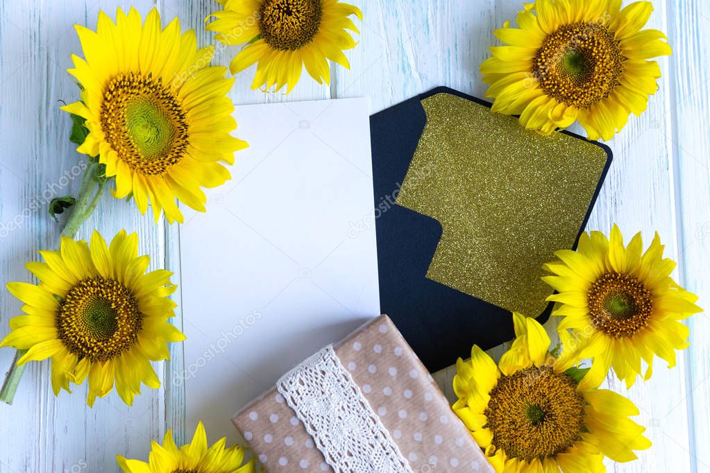 Template with envelope, sunflower flowers, gift box on a light wooden background. Banner for mailing with flowers of sunflower. Flat lay, top view.