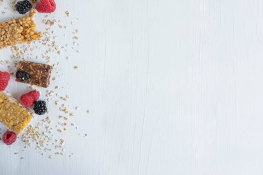 Beyaz ahşap arka planda granola ve yaban mersini, ahududu, yaban mersini ve yulaf ezmesi doğal meyveleri ile metin için çerçeve. Atıştırmalık ve kahvaltı için faydalı tahıl barları