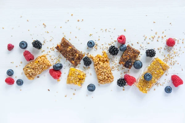 Frame for text with granola and natural berries of blueberries, raspberry, blackberry, blueberry and oatmeal on a white wooden background. Useful cereal bars for snacking and breakfast