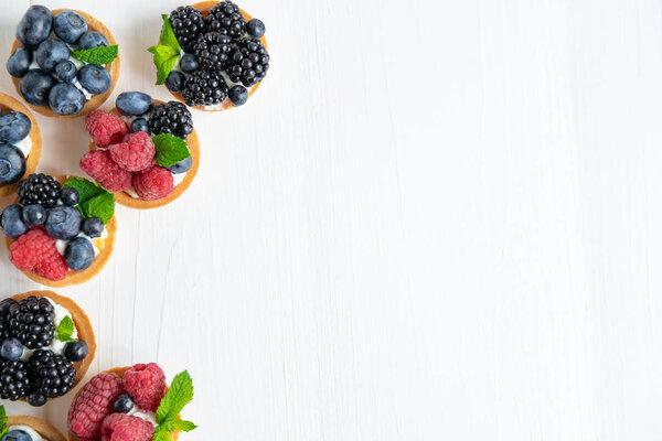 Фон с тарталетками. Ягодные тарталетки с пространством для копирования. Кексы с малиной, черникой и черникой на белом деревянном фоне. Рекламный баннер со сладостями. Вид сверху
