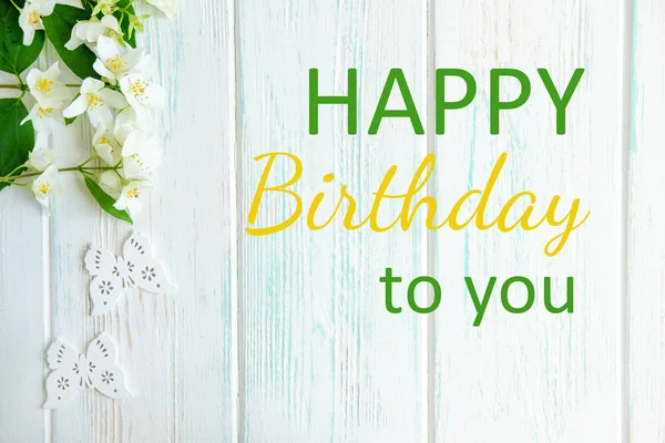 Greeting card, birthday banner with the inscription, jasmine flowers on a light wooden background. Happy Birthday to You. View from above