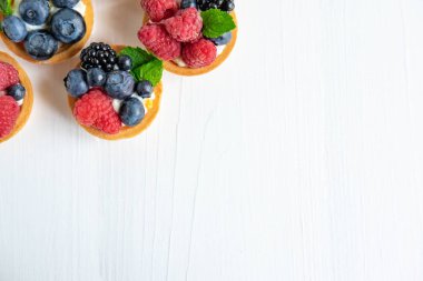 Beyaz ahşap arka plan üzerinde tartlets ile Fotoğraf desen. Marina, yaban mersini, nane yaprakları ile yaban mersini çilek ile Kek. Tatlılar üst görünümü ile Fotoğraf patern