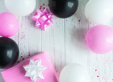 Doğum günü kartı arka planı için tasarım çerçevesi. Pembe, beyaz ve siyah balonlar açık ahşap arka planda bir hediye kutusu ile. Tebrik kartı tasarımı