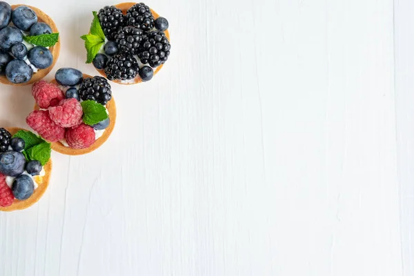 Photo pattern with tartlets on a white wooden background. Cakes with berries of marina, blueberry, blueberry with mint leaves. Photo patern with sweets — Stock Photo, Image