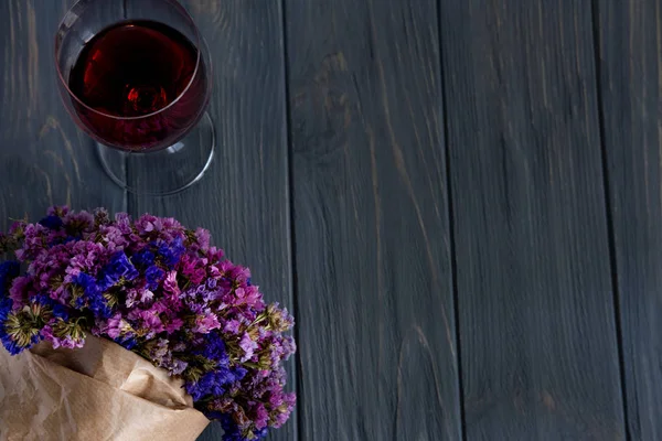 Ένα ποτήρι κόκκινο κρασί κοντινό, μαζί με ένα μπουκέτο αγριολούλουδων σε ένα γκρίζο ξύλινο φόντο. Πανό χαιρετισμού — Φωτογραφία Αρχείου