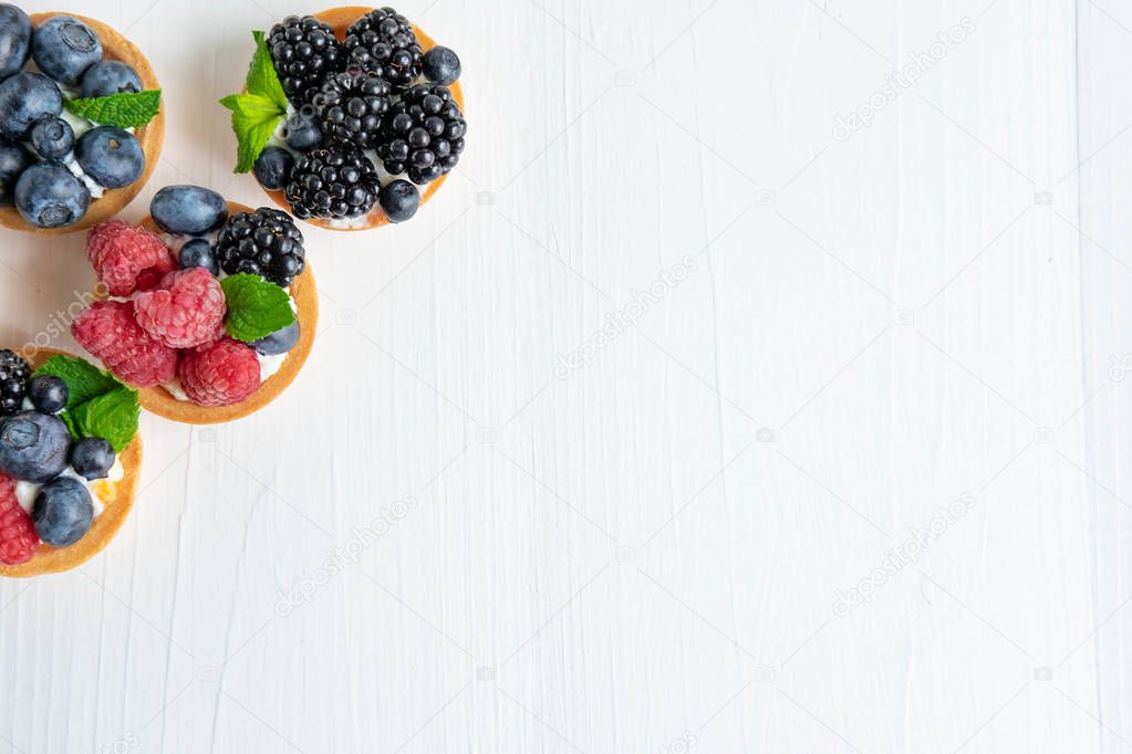 Photo pattern with tartlets on a white wooden background. Cakes with berries of marina, blueberry, blueberry with mint leaves. Photo patern with sweets