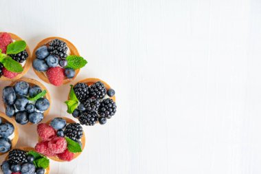 Ahududu, yaban mersini ve böğürtlenli tartlarla dolu bir arka plan. Güzel hamur işleriyle dolu metin için çerçeve. Hafif arkaplanda, yazıtlar için bir yeri olan tatlılar.