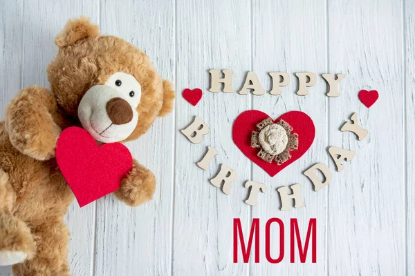 Happy birthday mom. Greeting card design for mom\'s birthday with a teddy bear and a heart. Flat layout, top view. Happy mother\'s day