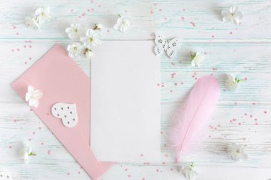 Hafif ahşap arka planda kiraz çiçekleriyle süslenir. Pembe zarflı bir mektup ve yazılacak bir yeri olan bir kalem..