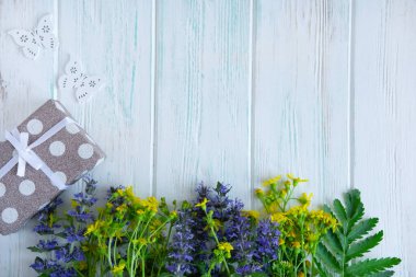 Yazlık kır çiçekleri, açık ahşap bir zemin üzerinde hediye kutusu ve yazıtlar için bir yer. Tebrik kartı için çiçek arkaplanı.