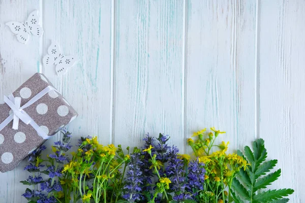 Yazlık kır çiçekleri, açık ahşap bir zemin üzerinde hediye kutusu ve yazıtlar için bir yer. Tebrik kartı için çiçek arkaplanı.