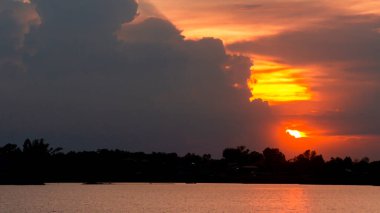 Güneş ufukta batıyor ve büyük bulutlar. Büyük bir gölün yanında.