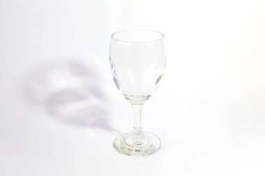 Beyaz arka planda berrak bir kadeh şarap serilir ve arkasında gri bir gölge parlar..