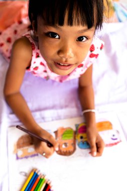 Yatağa resim çizen küçük bir kız. Maske takan insanlarla ilgili bir resim. Virüs yayıldığı için okul kapalı olduğu için evde çalıştıktan sonra Covid-19 virüsünü önlemek için.