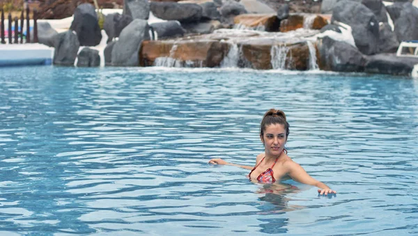 Mujer en el agua en una piscina con una cascada en el fondo . — Foto de Stock