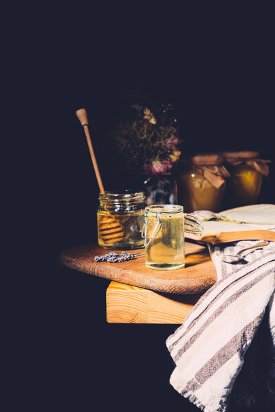 selective focus of various jars with honey and honey stick on black background