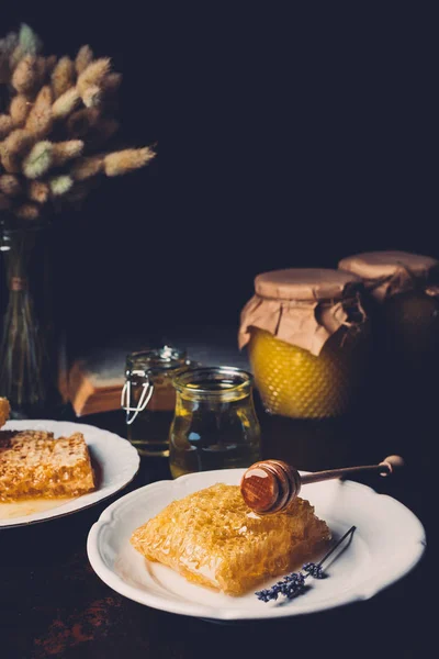 Selective focus of honeycombs on plates and jars with honey on black background — Stock Photo