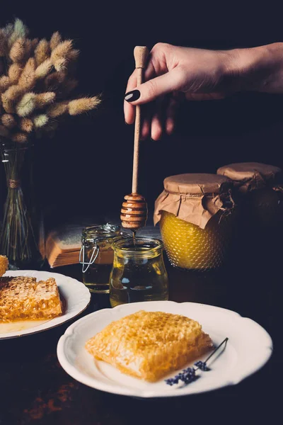 Immagine ritagliata di donna che mette il bastone di miele in vaso con miele su sfondo nero — Foto stock