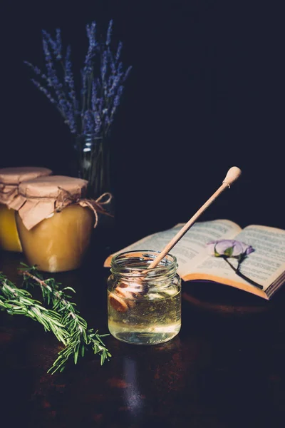 Selective focus of rosemary and honey stick in jar with honey on black background — Stock Photo