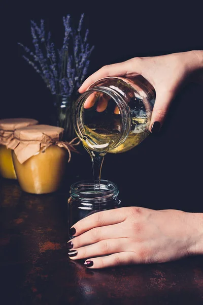 Cropped image of woman pouring honey into jar on black background — Stock Photo