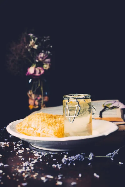 Close up view of honeycomb and jar with honey surrounded by petals on black background — Stock Photo