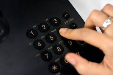 Vista en alto de una mano femenina marcando un marcando un marcando un numero en dispositivo fijo negro