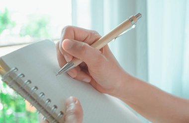 Kadın el üstünde beyaz defter doğa ışık ile pencere ve arka planda beyaz perde yazıyor.