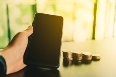 Kadın el işi yapmak için smartphone kullanarak ile iş finansal başarı kavramı. Tablo ve yeşil doğa bokeh zemin üzerine altın sikkeler.