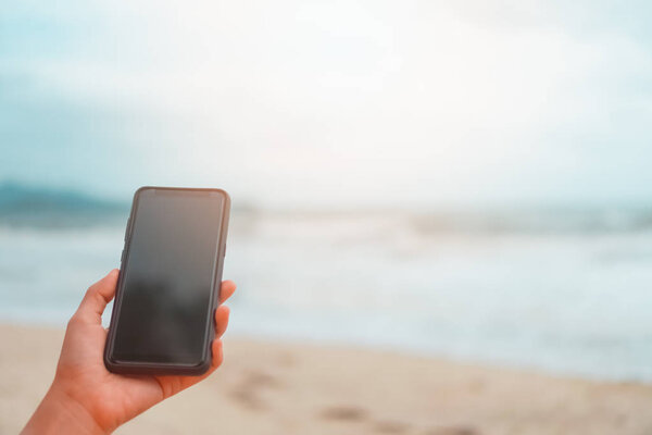 Женщина рука с помощью смартфона перед летним пляжем с красивым солнечным светом
.