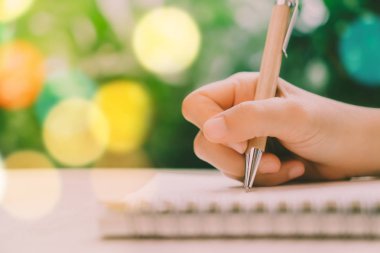 Renkli bokeh arkaplana sahip beyaz not defterine kadın eli yazma boşluğunu kopyala.